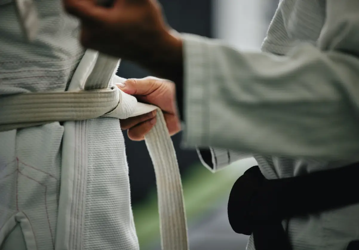 A black belt martial arts instructor helping tie a young martial arts student's white belt.